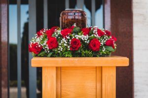 Funerary urn with ashes of dead and flowers at funeral. Burial urn decorated with flowers at memorial service on a wooden stand, sad and grieving last farewell to deceased person.